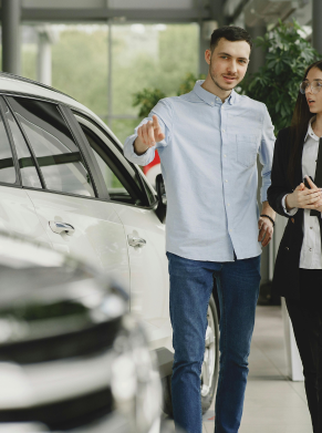 Man and woman standing next to a white car in a showroom, discussing details.