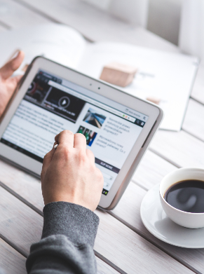 Person using a tablet with news articles next to a cup of coffee.