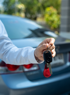 Hand holding car key fob and key near blue car.