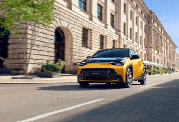 Yellow car driving past a historic stone building.