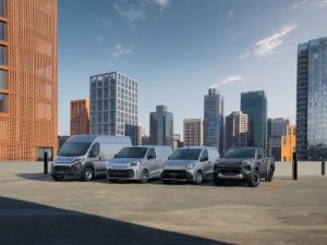 Lineup of four grey and silver vans parked on an open rooftop with city skyline in the background.