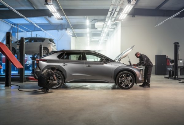 Two mechanics inspecting a silver car in a garage.
