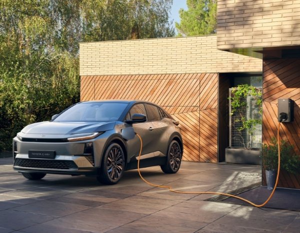 Toyota C-HR Plus charging in a driveway next to a modern building.