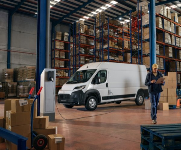 Electric van charging in a warehouse, worker with clipboard nearby.