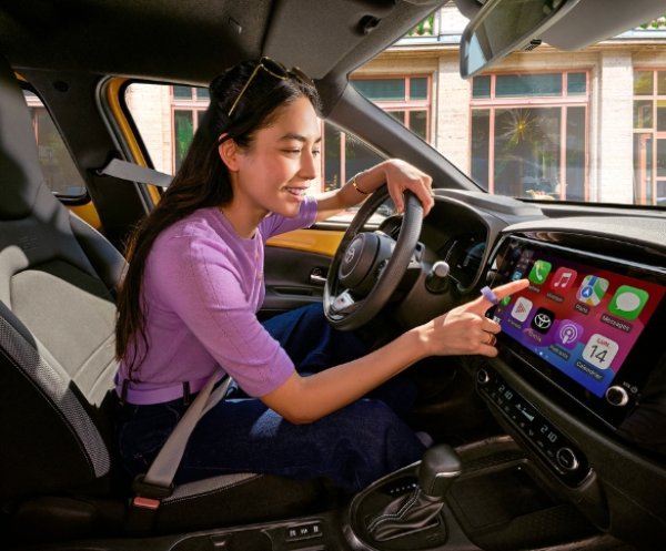 Person using a touchscreen dashboard in a parked yellow car.