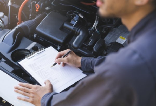 Mechanic with a clipboard inspecting a car engine.