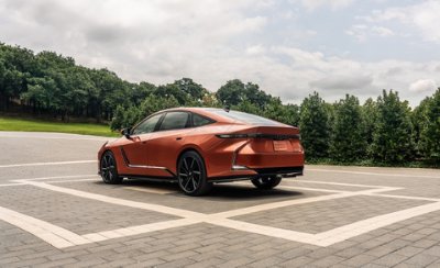 Orange futuristic car parked on paved area with trees in the background.