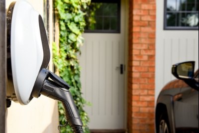 Electric vehicle charging at a wall-mounted charger near a brick wall and ivy-covered area.