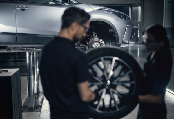 Two mechanics changing a car tyre in a workshop.