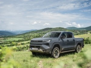 A dark pickup truck parked on a grassy hill with mountains in the background.