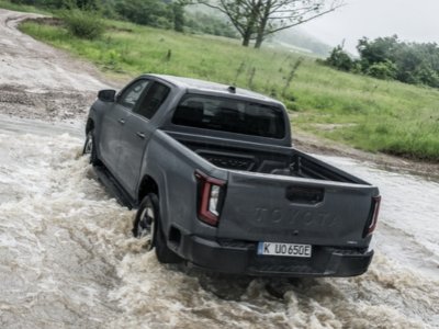 Grey pickup truck driving through shallow water on a rural path.