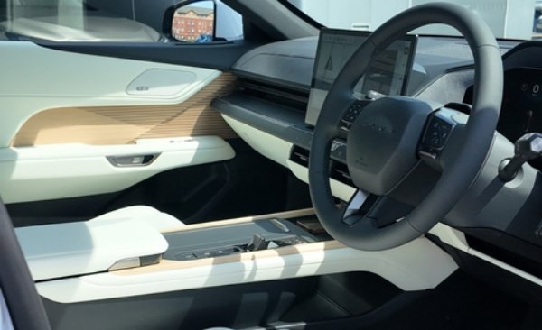 Car interior with a steering wheel, touchscreen display, and light wood-effect trim.