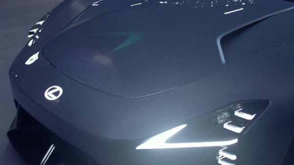 Close-up of the front of a dark Lexus car with illuminated headlights.