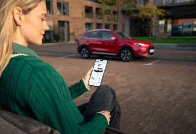 Woman using a smartphone app while sitting, red car parked in the background.