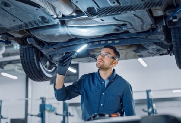 Mechanic inspecting underside of a car with a flashlight.