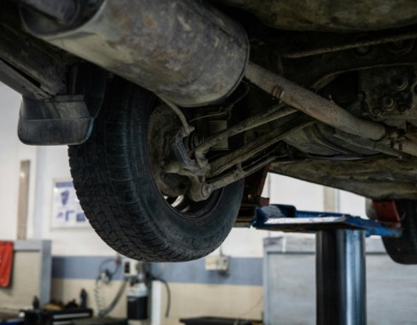 Car underside showing exhaust and rear wheel on a lift in a garage.