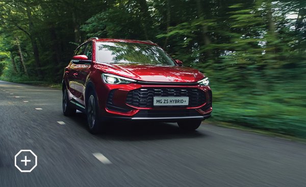 Red MG ZS Hybrid+ driving on a tree-lined road.