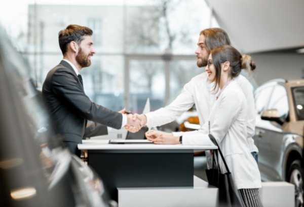 Salesperson shaking hands with a couple at a car dealership.
