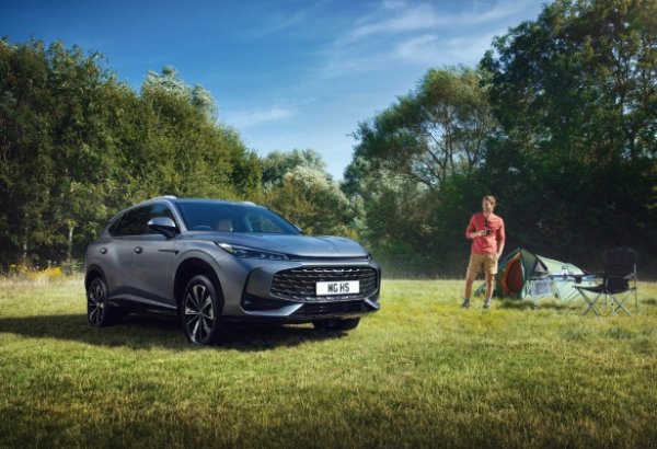 Silver SUV parked on grass with a man standing near a tent and camping chair.