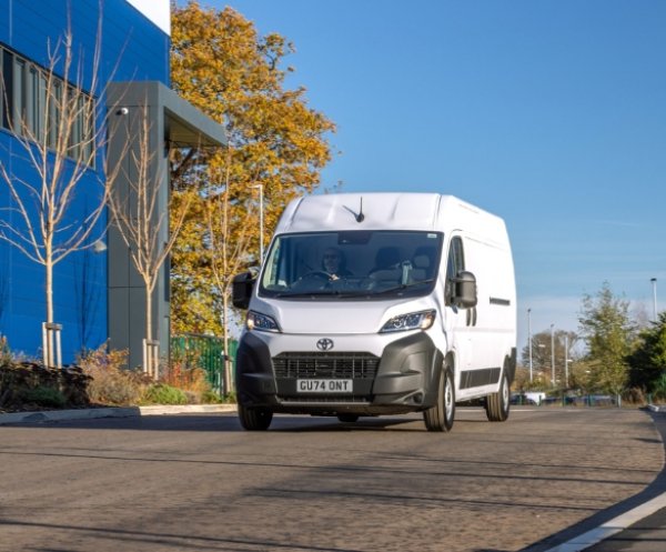 White van driving on a road near a building, registration GU74 ONT.