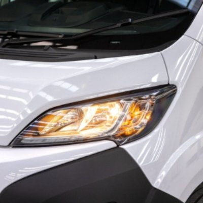 Close-up of a lit front headlamp on a white vehicle.