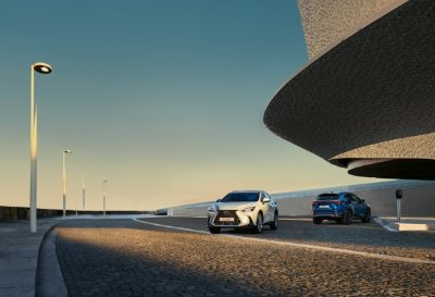 Two cars driving on a curved, cobblestone road near modern architectural structures.