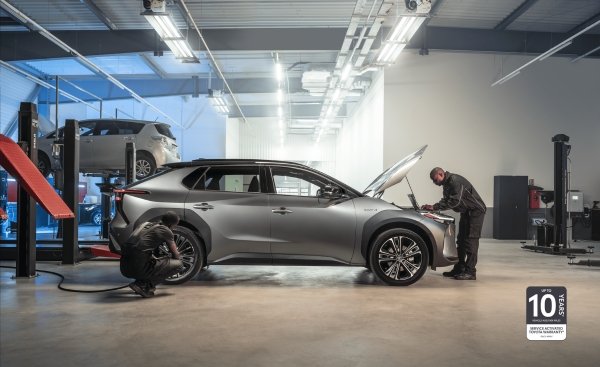 Two mechanics working on a silver car in a workshop.