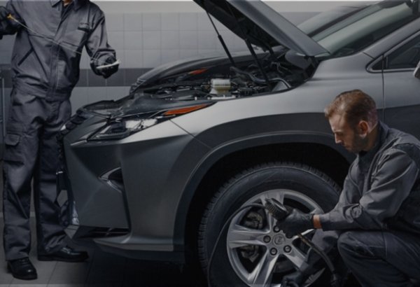 Mechanics working on a grey car with its bonnet open.