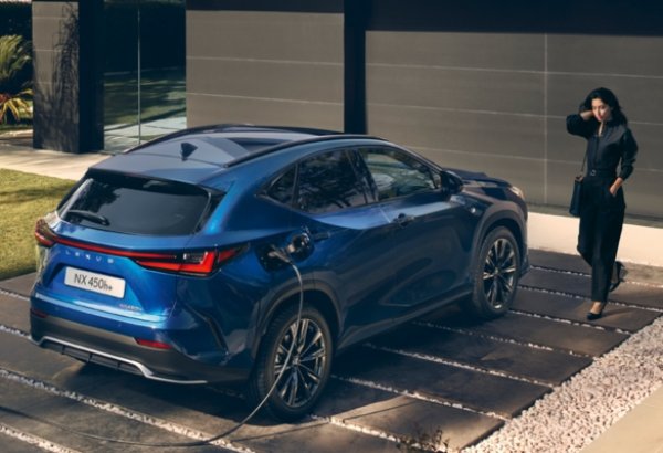 Blue electric car charging with a person standing nearby.