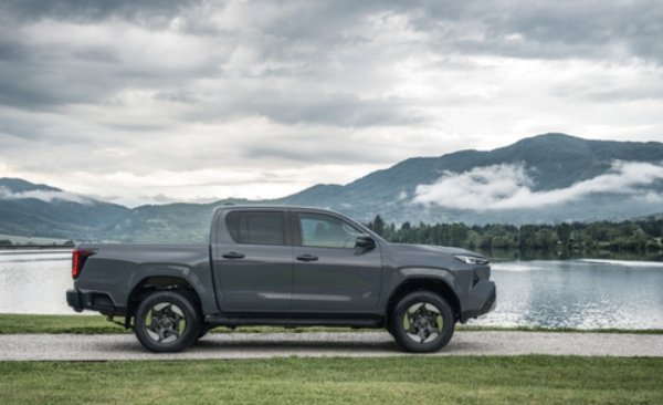A grey pickup truck parked beside a lake with mountains in the distance.
