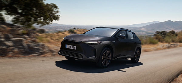 A black electric SUV driving on a rural road with hills in the distance.