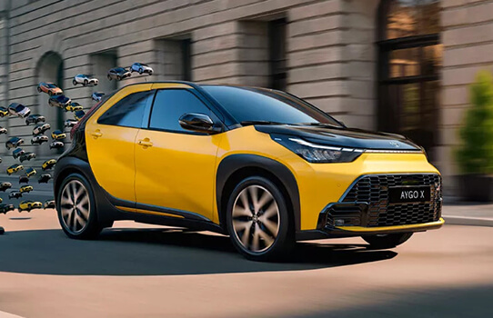 Yellow and black Aygo X car driving on a city street.