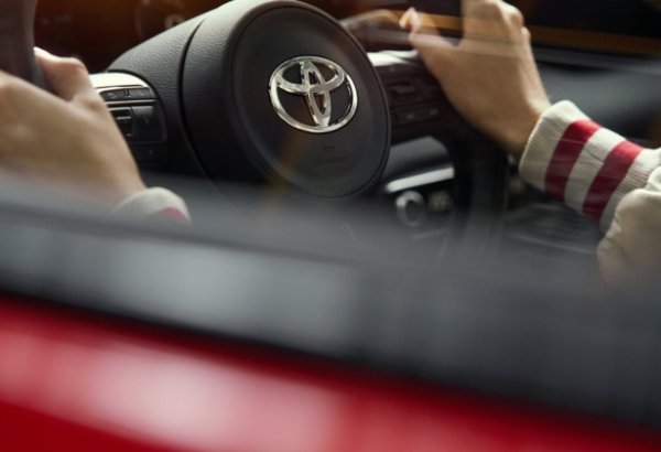 Close-up of hands on a Toyota steering wheel viewed through a car window.