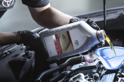 Mechanic pouring Toyota engine oil into a car engine using a funnel.