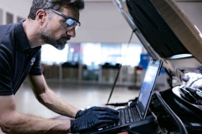 Mechanic using a laptop while inspecting a car engine.