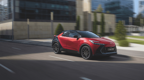 A red Toyota C-HR driving on a city street.