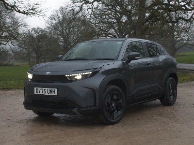 Grey SUV parked on a dirt road with trees in the background.