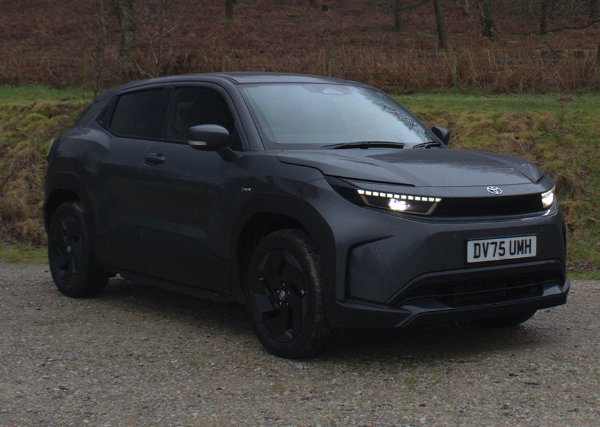 Dark-coloured SUV parked on a gravel path near woodland.