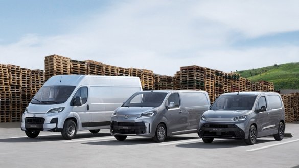 Three silver vans parked in a row beside stacked wooden pallets.