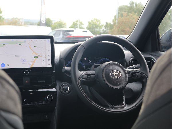 Car interior showing steering wheel and satnav display with map directions.