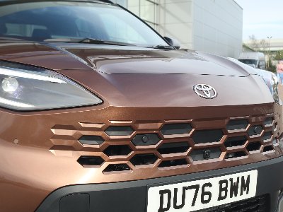 Close-up of a brown Toyota SUV front grille and headlights, with UK registration plate DU76 BWM.